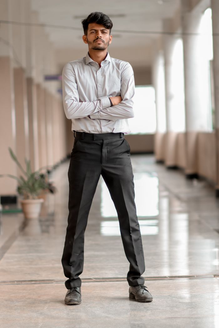 Portrait of a confident adult man standing in a modern corridor with arms crossed.